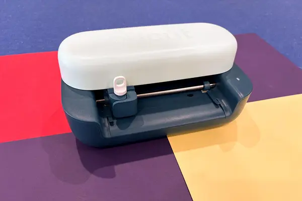 The compact Cricut Joy 2 sits on a clean desk next to various craft supplies like vinyl and cutting tools.